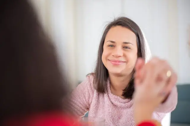 Nainen hymyilee lämpimästi toiselle naiselle, ilmentäen yhteyden ja ilon hetkeä, sosiaalinen introvertti.